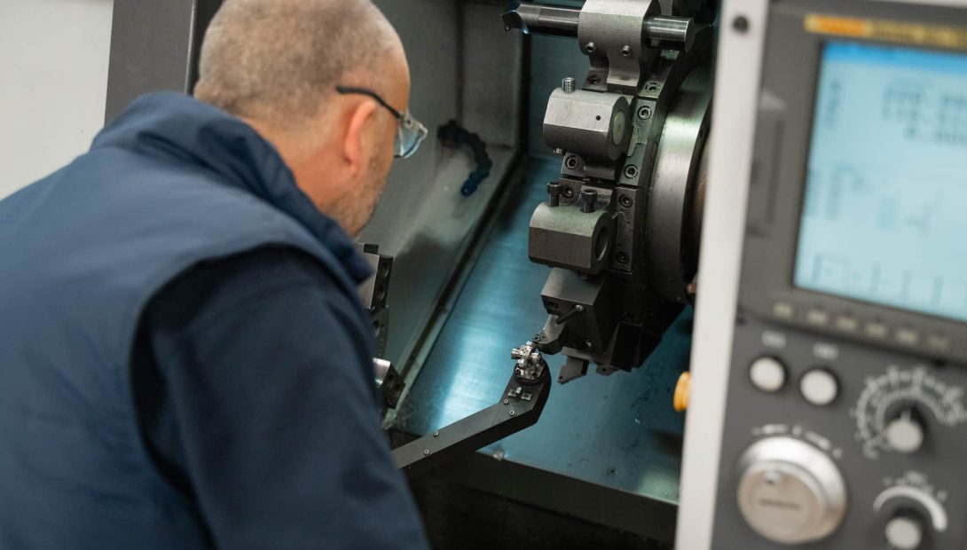 Engineer in safety glasses operating a CNC lathe with the tooling and control panel in view
